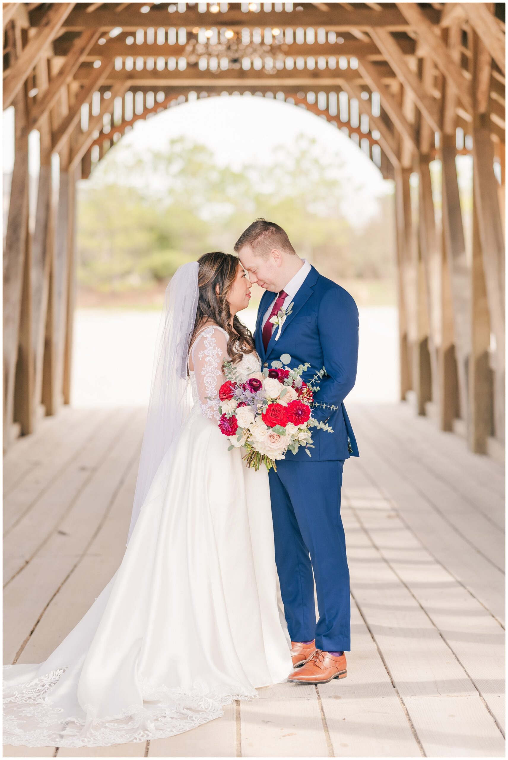 Bride and Groom pose on the covered wood bridge at Big Sky barn with beautiful red roses.