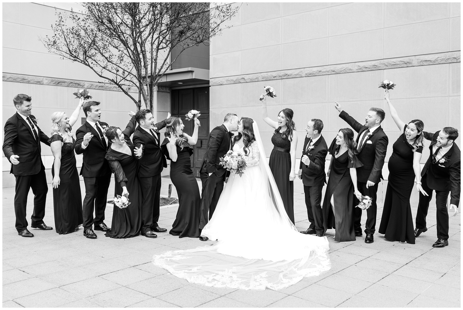 Wedding Party cheers on bride and groom as they kiss outside the church.