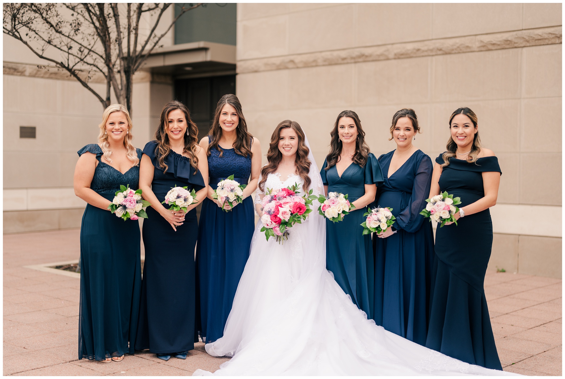 bride and bridesmaids wearing dark blue, pose for a photo with their bouquets.