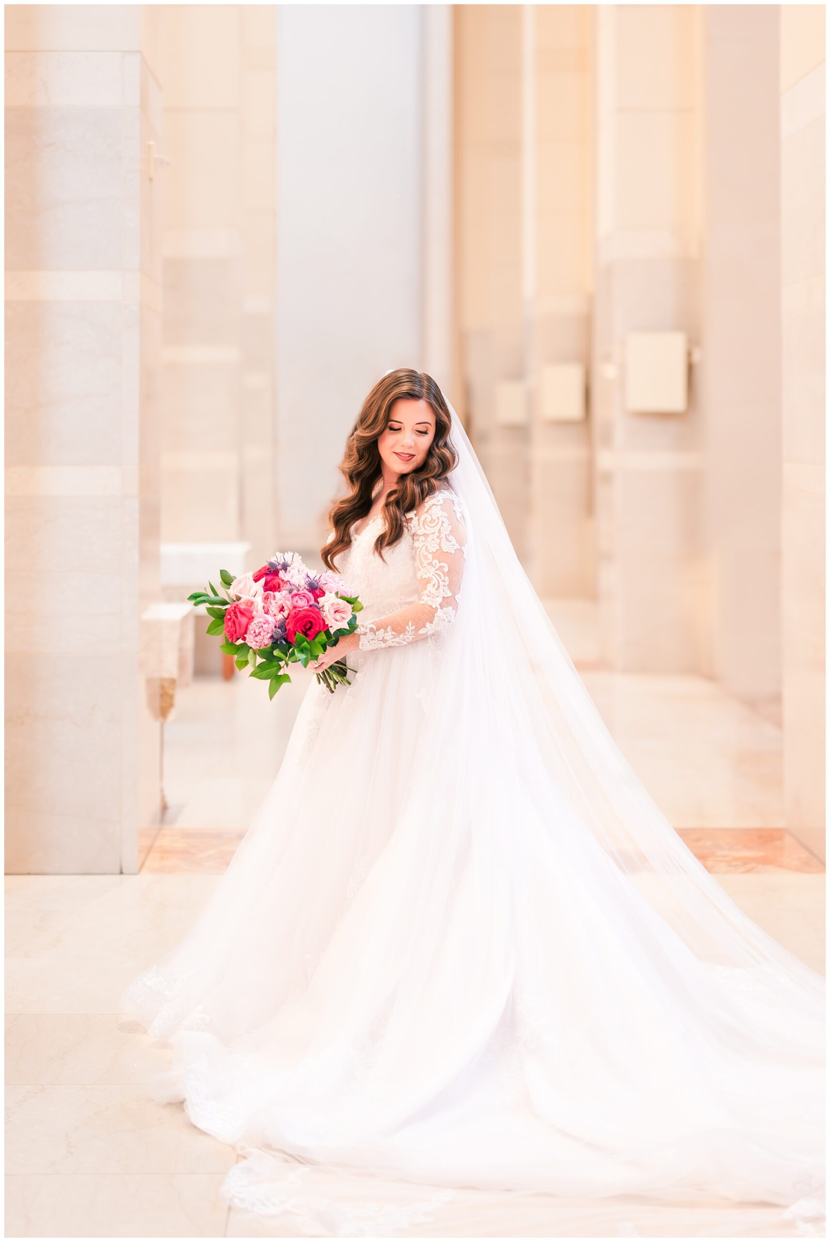 Bride in lace dress with long cathedral train and veil stops to look down at the Co Cathedral of Houston before her church wedding.