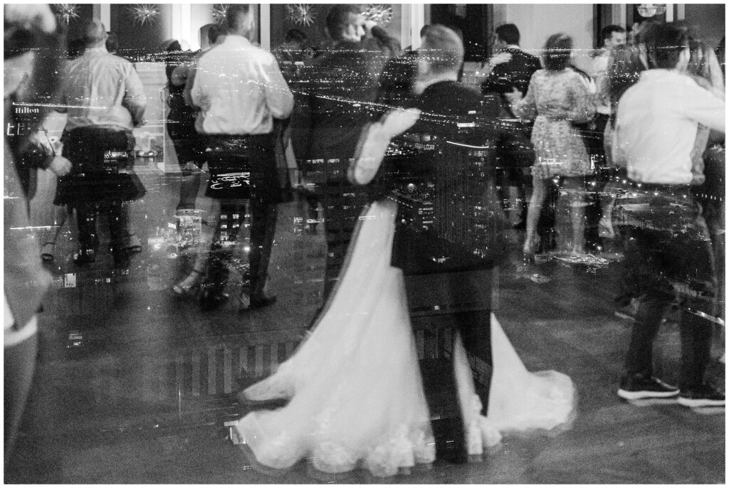 reflection of bride and groom dancing with the city of houston lights in the window at the Petroleum Club.