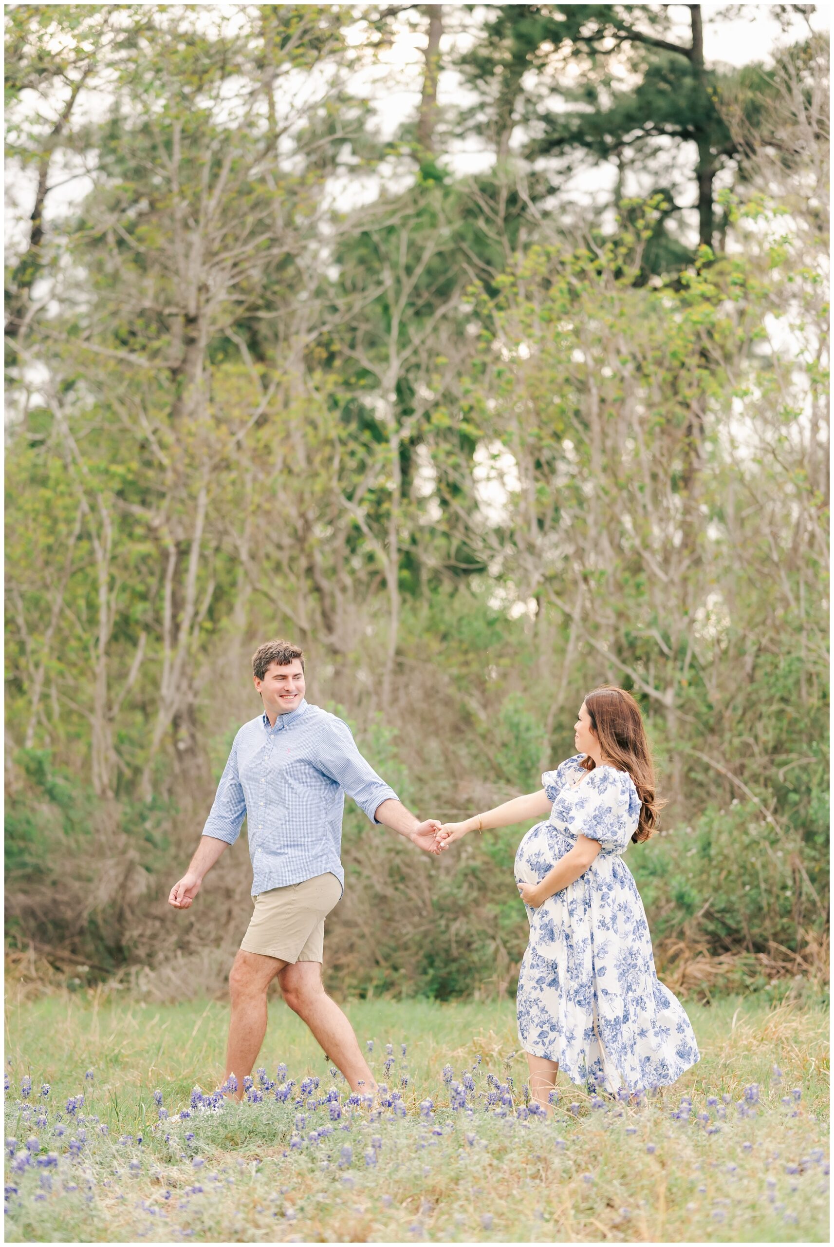 husband leads pregnant wife through the bluebonnets in The Woodlands.